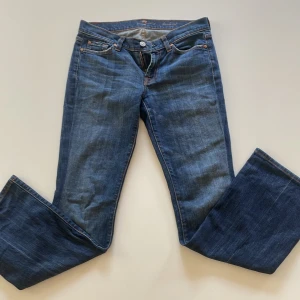 Blå bootcut jeans från Nudie - Snygga blå jeans från Nudie med klassisk bootcut-modell och låg midja. Jeansen har fem fickor, orangea sömmar och detaljerade bakfickor med Nudie-loggan. Tillverkade i mjukt denimtyg som sitter skönt och ger en avslappnad vibe.