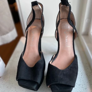 Svarta mocka klackar Jeffrey Campbell - Snygga svarta klackar från Jeffrey Campbell i mocka med öppen tå och kraftig plattform. Skorna har unik design med utskurna sidor och bred klack som ger extra höjd och stabilitet. Perfekta för dig som vill sticka ut med en edgy och trendig look.