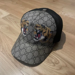 Gucci keps med tigertryck och GG-mönster - Tjena säljer nu min Gucci keps storlek S, den är i utmärkt skick som ni kan se på bilder som ni ser på justeringsremen så har den aldrig öppnats jag har aldrig justerat den på något sätt den har suttit på samma plats, jag ska bara klar göra att en keps som denna som har slutat säljas ifrån Gucci store och i en sån bra skick är guld, varför jag säljer den är för att jag ej använder den längre. Kvitto, box, dustbag medföljer.                                                Hoppas ni hör av er.🙂