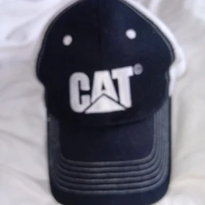 Svart och vit keps från CAT - Snygg svart och vit keps från CAT med klassisk logga framtill. Kepsen har böjd skärm, vit mesh baktill för extra ventilation och justerbar snapback. Perfekt för dig som gillar streetwear eller vill ha en cool accessoar till vardagslooken.