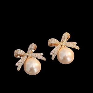 Guldiga örhängen med pärlor och rosett - Supersöta örhängen i guld med gnistrande rosetter och stora vita pärlor. Perfekta för dig som vill ha en elegant och söt detalj till din look. Rosetterna är täckta av små glittrande stenar som ger extra bling.