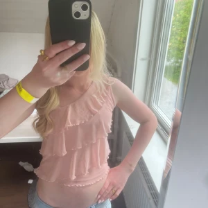 Ljusrosa one shoulder volangtop - Supersöt ljusrosa topp med one shoulder och flera lager volanger. Toppen är axelbandslös på ena sidan och har en mjuk, flowy känsla. Perfekt för dig som gillar romantisk och feminin stil. Säljs då den inte kommer till användning längre. Xxs= 152 💞