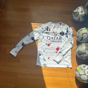 PSG långärmad fotbollströja Nike S - Säljer en långärmad Paris Saint-Germain fotbollströja från Nike i storlek S. Tröjan är vit med blå och röda borstade mönster, PSG-emblem på bröstet och Qatar Airways-tryck. Tillverkad lätt och ventilerande , perfekt för träning eller match.