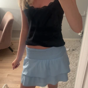 Ljusblå volangkjol från Gina  - Supersöt ljusblå kortkjol från Gina. Kjolen är i mjuk bomull och har en flowy känsla som är perfekt för varma dagar. Enkel att matcha med både toppar och sneakers.