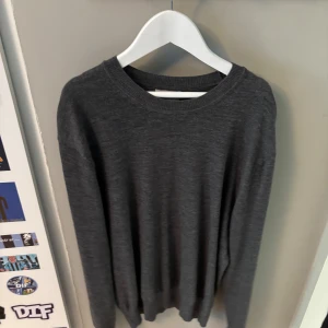 Mörkgrå stickad tröja från Sandö - Mörkgrå stickad tröja från Sandö i klassisk modell med rund halsringning och långa ärmar. Perfekt för lager-på-lager och enkel att matcha med jeans eller chinos. Mjuk och skön känsla, passar dig som gillar stilrena basplagg.