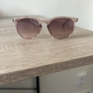 Beiga transparenta solglasögon - Snygga solglasögon med transparent rosa bågar och mörka glas. Klassisk rundad form som ger en cool vibe. Perfekta för att lyfta din stil under soliga dagar.