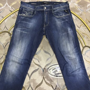 Replay Anbass Hyperflex jeans blå - Snygga Replay Anbass Hyperflex jeans i mörkblå tvätt med slitningar och kontrastsömmar. Klassisk femficksmodell med logga på bakfickan och stretchigt material för extra komfort. Perfekta för dig som gillar en modern och avslappnad look.