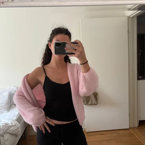 Ljusrosa stickad  kofta från Lindex - Supermjuk och fluffig ljusrosa stickad väst från Lindex. Modellen är öppen framtill och har en avslappnad, lite oversized passform med breda ärmhål. Perfekt att slänga över en topp för en söt och chill look.