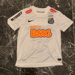 Santos Neymar Jr matchtröja Nike M - Vit Santos fotbollströja från Nike med Neymar Jr och nummer 11 på ryggen. Klassisk design med svarta och orangea tryck, klubbmärke på bröstet och flera sponsorer. Tillverkad i lätt Dri-FIT-material som andas, perfekt för fotbollsplanen.