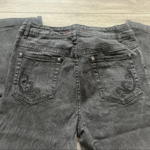 MörkGråa jeans - Snygga svarta jeans med bootcut passform och broderade detaljer på bakfickorna. Jeansen har klassisk femficksdesign och är tillverkade i denim. Perfekta för dig som gillar en stilren look med en twist.