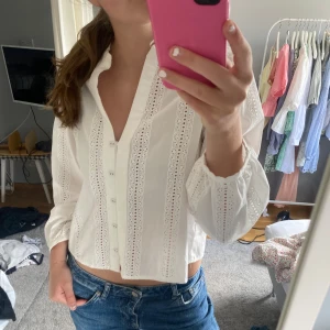 Vit broderad blus från Zara - Superfin vit blus från Zara med broderade spetsdetaljer och knappar framtill.  Den är långärmad med lite puffig touch och v-ringning. Perfekt att styla med jeans för en fräsch look. Nästan nyskick, använd några få gånger. 
