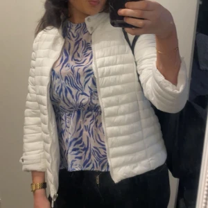 Vit quiltad pufferjacka - Snygg vit pufferjacka med quiltad design och dragkedja framtill. Jackan har en stilren look med ståkrage och trekvartärmade passform. Perfekt för dig som vill ha en fräsch och modern jacka till vardags/sommarkväll.😃☀️