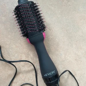 Revlon One-Step Volumizer hårborste - Revlon One-Step Volumizer är en svart och rosa elektrisk rundborste med borst i plast och piggar med rosa toppar. Perfekt för att styla och ge volym till håret med både borst och varmluft i ett enda verktyg. Ergonomiskt handtag och lång sladd.