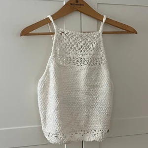 Vit virkad linnetopp från Hollister - Superfin vit virkad linnetopp från Hollister med smala axelband och snygg knytning i ryggen. Toppen har virkade detaljer upptill och nertill som ger en boho-vibe. Perfekt till sommaren och lätt att matcha med jeans eller kjol.