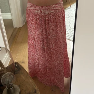 Rosa mönstrad långkjol - Säljer en rosa långkjol med paisleyinspirerat mönster. Kjolen har bred midja med fina detaljer och ett luftigt, flowy fall. Perfekt för dig som gillar boho-vibbar och vill ha något bekvämt men ändå snyggt. Materialet känns lätt och svalt.