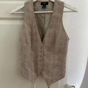 Beige rutig väst från H&M - Snygg beige väst från H&M med diskret rutigt mönster och v-ringning.