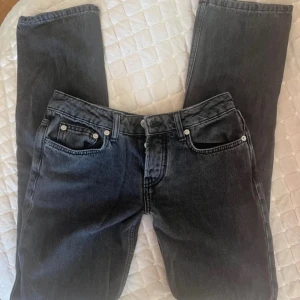 Svarta lågmidjade jeans - Säljer ett par svarta jeans med låg midja. Jeansen har klassisk femficksdesign, silverfärgade nitar och knappar. Snygg, enkel look som passar till det mesta. Materialet är jeans och färgen är mörk svart.