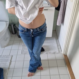Blå bootcut jeans från gina tricot - Säljer ett par klassiska blå bootcut jeans från Gina tricot  med låg midja. Jeansen har fem fickor, snygga detaljer på bakfickorna med knappar och är tillverkade i mjukt denim. Perfekta för dig som gillar en avslappnad men ändå trendig look.