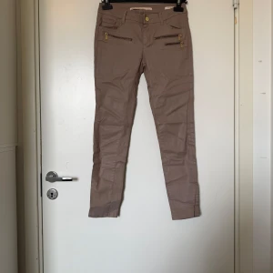 Beige skinny byxor med dragkedjor - Snygga beige skinny byxor från Zara  med guldiga dragkedjor framtill som cool detalj. Byxorna har normal midja, smal passform och är tillverkade i bomullsmix. Perfekta för dig som gillar stilrena men ändå edgy plagg. Storlek 36/S. Mycket fint skick, jag hittar inga synliga anmärkningar eller defekter. 
