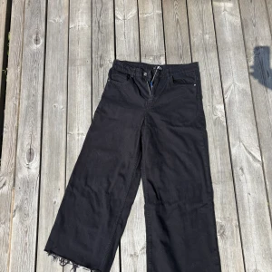 Svarta wide jeans från Zara TRF - Svarta jeans från Zara TRF med breda ben och råa, fransiga benslut. Klassisk femficksmodell med dragkedja och knapp. Snyggt loose fit och hög midja