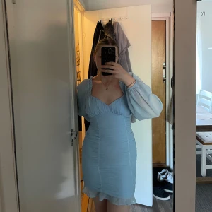 Ljusblå kort klänning från NLY Trend - Supersöt ljusblå kort klänning från NLY Trend med puffiga långärmar, rynkade detaljer och volangkant nertill. Klänningen har en smickrande v-ringning och är tillverkad i 100% polyester. 