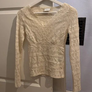 Krämvit spetsblus från Vila - Säljer en elegant krämvit spetsblus från Vila i storlek XS. Blusen har en v-ringad design med långa ärmar och ett vackert spetsmönster. Perfekt för att ge en romantisk touch till din outfit. Aldrig använd.