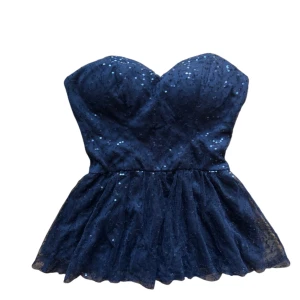 Svart paljettprydd tubtopp - Snygg svart tubtopp med glittrande paljetter och en volangdetalj nedtill. Perfekt för en festlig kväll när du vill sticka ut. Toppen är axelbandslös och har en figurnära passform.Några paljetter kan va borta. 