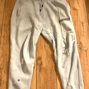 Grå mjukisbyxor från Hoodrich - Säljer ett par grå mjukisbyxor från Hoodrich med elastisk midja och dragsko. Byxorna har tryckt logotyp på benet och är perfekta för en avslappnad stil. De har en bekväm passform och är gjorda i mjukt material.