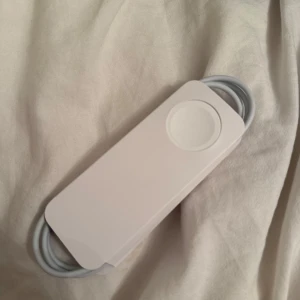 Magsafe laddare för applewatch  - Säljer en vit laddare för smartklocka med en rund laddningsyta och en sladd som kan lindas runt enheten. Perfekt för att hålla din klocka laddad och redo. Enkel och stilren design.