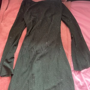 Grön glittrig klänning - Snygg grön klänning med glittrande detaljer. Den har en elegant passform och långa ärmar, perfekt för en festlig kväll. Klänningen är gjord i ett bekvämt material som ger en fin siluett.