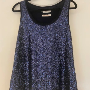 Blå glittrig topp - Säljer en snygg blå glittrig topp med paljetter. Den är ärmlös och har en rund halsringning och är i en loose passform ✨ 