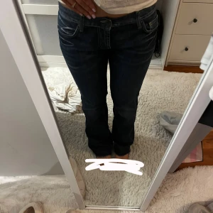 Mörkblå jeans från Red Monkey - Snygga mörkblå jeans från Red Monkey med klassisk femficksdesign och kontrastsömmar. Jeansen har en rak passform och låg midja, perfekt för en avslappnad stil. Märkesdetaljer på bakfickorna och en läderpatch på baksidan av midjan ger en extra touch.