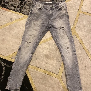 Grå jeansbyxor från FSBN - Snygga grå jeansbyxor från FSBN med slitna detaljer. Byxorna har en modern look med en tight passform och är perfekta för en trendig stil. De har en klassisk femficksdesign och dragkedja.