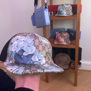 Blommig keps med Gucci-mönster - Snygg keps med ett klassiskt Gucci-mönster kombinerat med ett blommigt tryck i blått och vitt. Perfekt för att ge din outfit en lyxig touch. Kepsen har en justerbar rem baktill för bästa passform. Pris mellan 400 till 100 alla kepsar stolen s till L