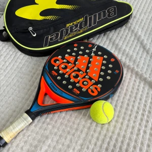 Padelväska från Bullpadel och Padelrack - Säljer två Padelrack och en svart och gul padelväska från Bullpadel. Väskan har en dragkedja och ett stort fack för att förvara padelracket och tillbehör. Perfekt för att hålla utrustningen organiserad och skyddad. Lätt att bära med sig till och från padelbanan.