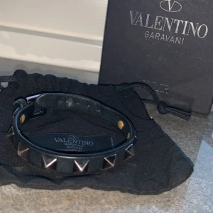 Svart Valentino Garavani armband - Snyggt svart armband från Valentino Garavani med silverfärgade pyramidnitar. Armbandet har ett justerbart spänne och kommer i originalförpackning. Perfekt för att ge en edgy touch till din stil. Nypris: 3085 kr Mitt pris: 1050 kr Skick: 8,5/10 Allt og med- Kvitto, box och dustbag. Hör av er kring frågor!😁