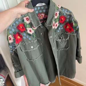 Army jacket - En grön army jacket med fina blommor på framsida o baksida! Köpt från two angels, använd fåtal gånger, sp gott som ny! Går att vika upp ärmarna, lite oversized men passar mig som brukar ha strl 36. Nypris 899kr