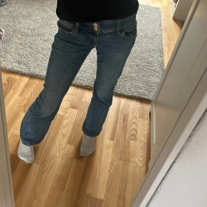 Blå jeans från Gina Tricot - Snygga blå jeans från Gina Tricot med en klassisk design. De har en lågmidjad passform och raka ben. Perfekta för en avslappnad stil. Jeansen har två knappar och dragkedja.