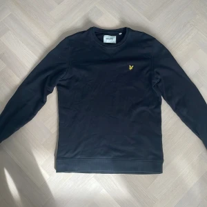 Svart tröja från Lyle & Scott - Säljer en stilren svart tröja från Lyle & Scott med deras ikoniska gula logga på bröstet. Tröjan är långärmad och tillverkad i ett mjukt material som ger en bekväm passform. Perfekt för en avslappnad look.