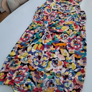 Talking French (Siden) - Säljer en färgglad blommig klänning i siden med en mix av blå, rosa, gul och lila nyanser. Klänningen är ärmlös och har en bekväm passform, perfekt för sommarens festligheter. 🌸