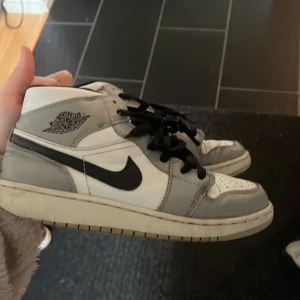 Nike Air Jordans i grått och vitt - Snygga Nike Air Jordans i en stilren kombination av grått och vitt. Skorna har en klassisk design med svart snörning och den ikoniska Nike-loggan på sidan. Perfekta för dig som vill ha en tidlös sneakerstil.