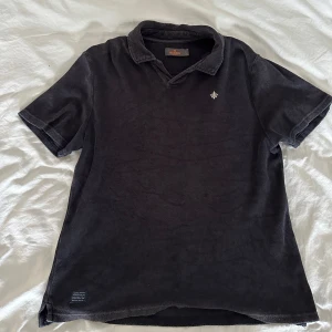 Marinblå frotté t-shirt från Morris - Säljer en svart frotté t-shirt från Morris med korta ärmar och en liten broderad detalj på bröstet. Perfekt för en avslappnad stil. T-shirten har en klassisk krage och är i storlek M.