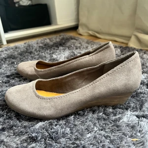 Beige mocka ballerinaskor - Snygga beige ballerinaskor i mocka med en låg kilklack. Perfekta för en stilren look och bekväma att bära hela dagen. De har en rundad tå och en diskret design som passar till många olika outfits.