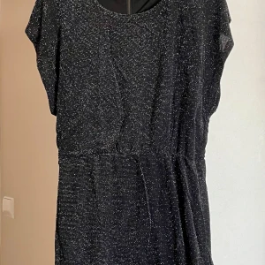 Svart glittrig klänning från Soaked in Luxury - Snygg svart klänning från Soaked in Luxury med glittrande detaljer. Perfekt för en kväll ute! Klänningen har en rund hals och korta ärmar.