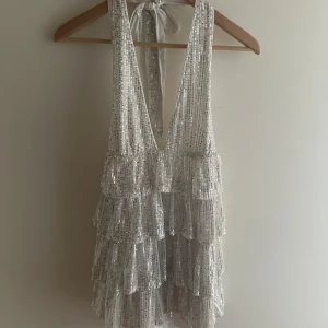Glittrig silverklänning med volanger - Intressekoll på en fantastisk glittrig silverklänning med djup v-ringning och volanger. Klänningen har en öppen rygg med knytband i nacken. Perfekt för fest och andra tillställningar💕passar allt från XS-L då man kan ändra med banden. 