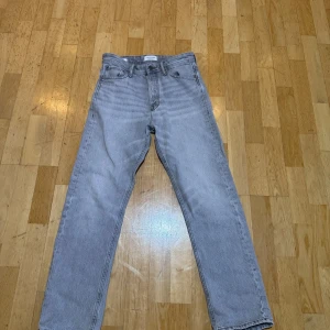 Grå jeans från Jack & Jones - Snygga grå jeans från Jack & Jones med klassisk design. De har en rak passform och är tillverkade i ett slitstarkt denimtyg. Perfekta för en avslappnad stil. Det har tyvärr ett litet hål(sista bilden) Man bör förstärka i grenen vid köp.
