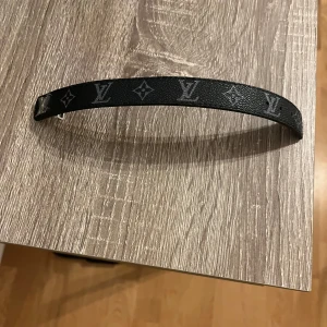Svart armband från Louis Vuitton - Snyggt svart armband från Louis Vuitton med det klassiska monogrammönstret. Tillverkat i Spanien, bältet har en elegant design med en diskret spänne. Perfekt för sommaren