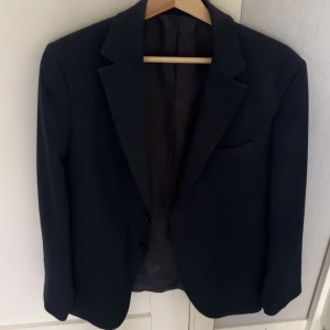 Mörkblå kavaj från Riley! - Elegant svart kavaj från Riley, perfekt för formella tillfällen. Kavajen har en klassisk design med två knappar framtill och en stilren krage. Passar utmärkt för både höst och vinter. Tillverkad i ett material som ger en sofistikerad look. Endast använd vid ett tillfälle! 