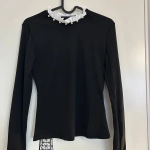Svart långärmad topp med pärldetaljer från SHEIN  - Jättefin svart långärmad topp med vit volang och pärlor vid halsringningen och ärmslut från SHEIN i storlek XS. Aldrig använd. 