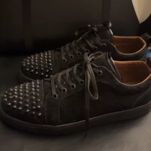 Svarta sneakers med nitar - Snygga svarta sneakers med nitar på tåpartiet och svarta snören. Skorna har en röd sula som ger en cool kontrast. Perfekta för att ge din outfit en edgy touch.